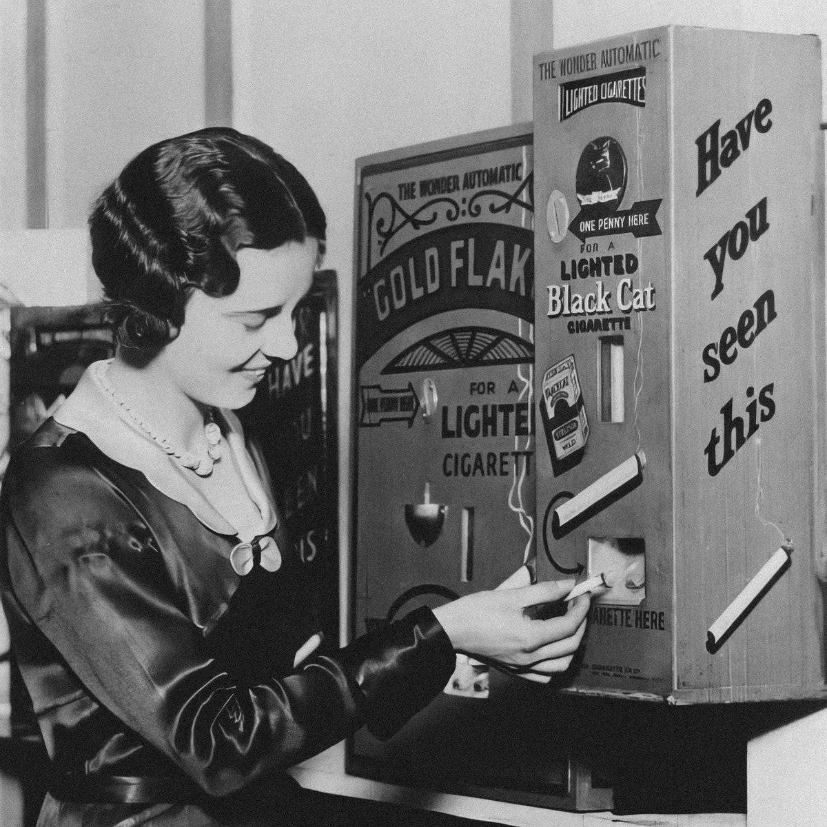 A woman using a vending machine dispensing lit cigarettes for a penny, England, 1931