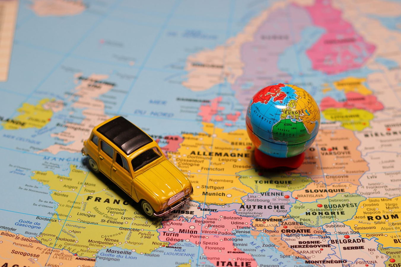 A yellow toy car and a small globe sitting on a map of Europe